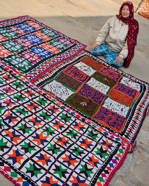 artist Ai Kijima sits on the ground next to several large quilts