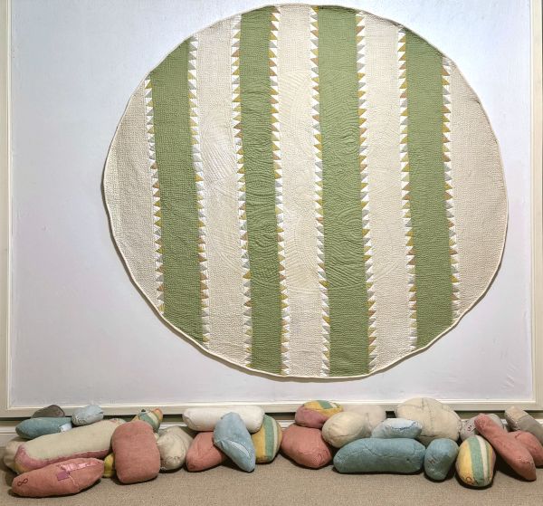 Judy Martin - The Beauty of the Green Earth with Mothering Bundles (a green and white striped circular quilt hangs above quilted rock-like bundles)