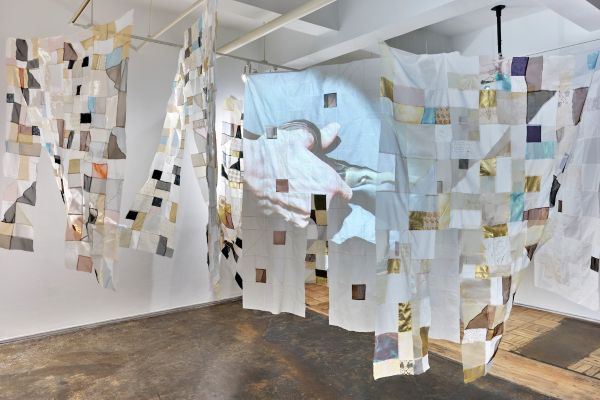 Holly Wong, Mending Body/Mending Mind, Fiber installation with 2 channel video & sound, Photo credit: Matthew Sherman (installation of patchwork hangings throughout a room. A hand with scissors is projected on one of them)
