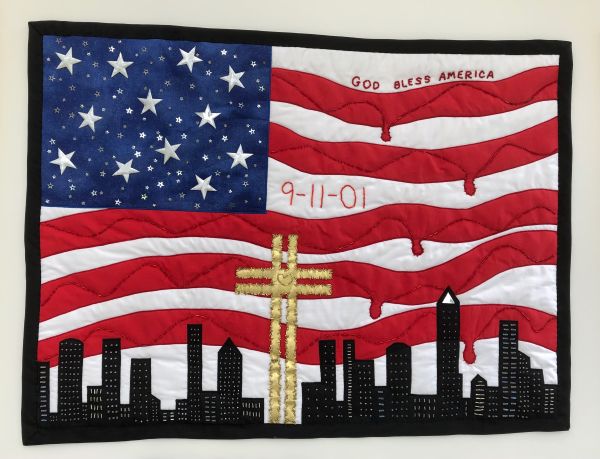 Susan Hoppenworth - 25 Years - 9/11 Remembered (the NYC skyline over an edited American flag that reads "God Bless America" and "9-11-01". A golden cross with heart is in the center and the red stripes of the flag are dripping)
