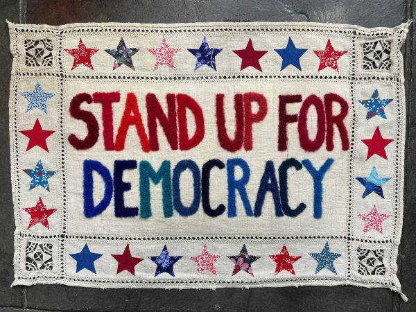 Stand Up For Democracy by India Tresselt (stitched sign that says stand up for democracy in red and blue. It is bordered by red, white, and blue stars)
