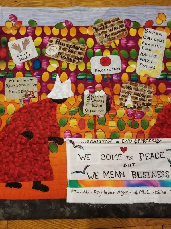 Glendora Simonson - We Come in Peace ... But We Mean Business (a quilt showing a black figure wearing a handmaid's tale outfit walking through a field of easter eggs with various protest signs "our bodies wombs eggs ourselves" "super callous fragile ego racist nazi potus" "no justice no peace no racist police" "humpty was pushed" a sign at the front says "coalition to end oppression we come in peace but we mean business #timesup righteous anfer #me2 divine"