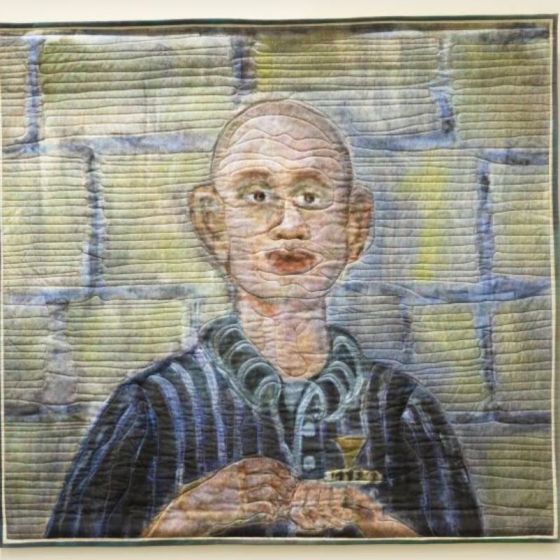 Colleen Ansbaugh - Szajna (quilted portrait of a bald man in a striped shirt in front of a brick wall)