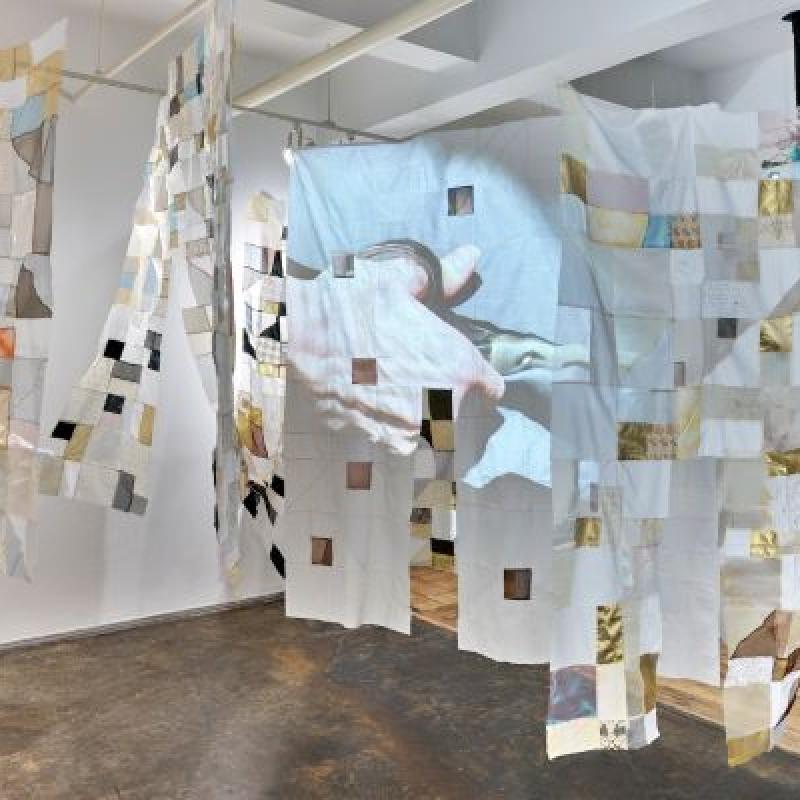 Holly Wong, Mending Body/Mending Mind, Fiber installation with 2 channel video & sound, Photo credit: Matthew Sherman (installation of patchwork hangings throughout a room. A hand with scissors is projected on one of them)